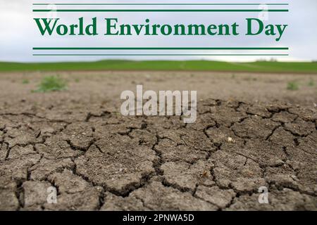 Ein gerissener Boden mit einem grünen Feld im Hintergrund. Dürrewasser und Klimakrise.Weltumwelttag am 5. juni Stockfoto