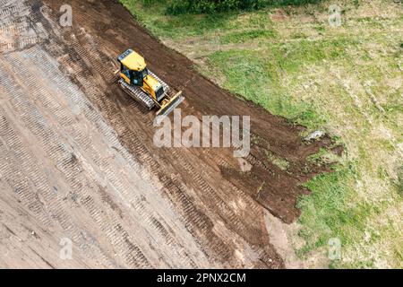 Der gelbe Kettendozer führt Erdbauarbeiten auf der Baustelle durch. Luftaufnahme von der fliegenden Drohne. Stockfoto