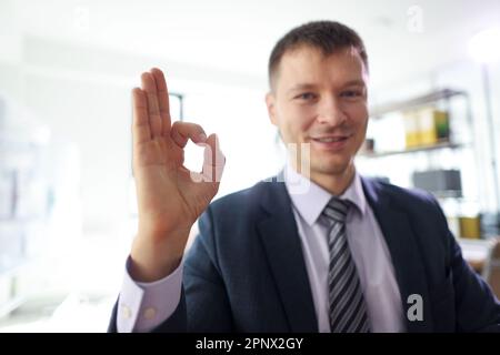 Ein lächelnder Geschäftsmann zeigt das "OK" -Schild im Büro Stockfoto
