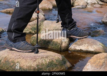 Trekker überquert einen kleinen Bach, der auf Felsen läuft Stockfoto