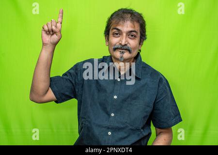 Der gut gekleidete Geschäftsmann in einem schwarzen Hemd zeigt mit der rechten Hand nach oben auf einen grünen Hintergrund und strahlt Selbstvertrauen aus Stockfoto