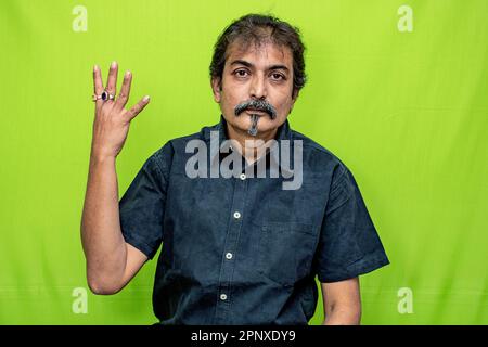 Ein kluger Gentleman in schwarzem Hemd zeigt „vier“ mit den Fingern seiner rechten Hand, die auf einem grünen Hintergrund stehen Stockfoto
