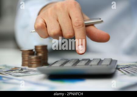 Nahaufnahme männlicher Hände zählt auf Taschenrechner und Münzstapel auf dem Tisch Stockfoto