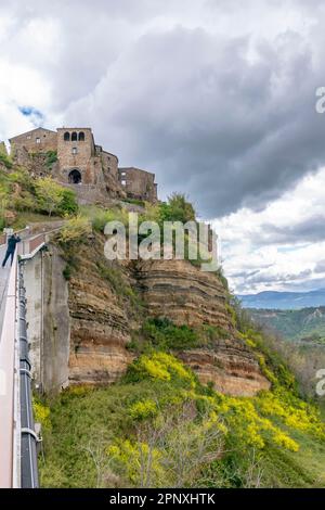 Ein Mann lehnt sich über die Brücke, um die sterbende Stadt Civita di Bagnoregio, Italien, unter einem dramatischen Himmel zu fotografieren Stockfoto