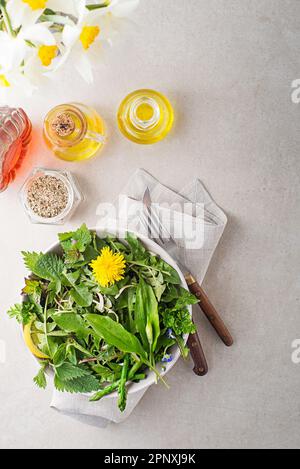 Gesunder Salat mit Frühlingspflanzen und Kräutern. Löwenzahn, wilder Knoblauch, Spargel, Blumen und Nesseln auf hellem Tischhintergrund Stockfoto