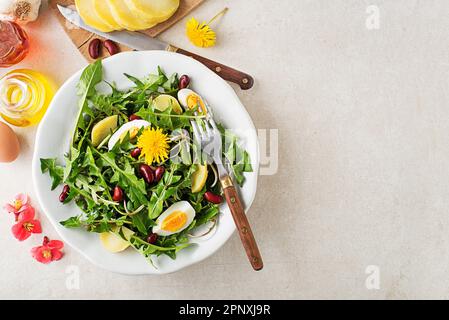 Löwenzahnsalat mit Eiern, Kartoffeln und Bohnen auf hellen Tischhintergrund Stockfoto