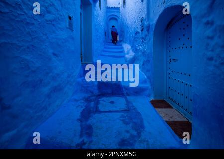 Silhouette einer Dame, die die blaue Treppe in einer Gasse in der Stadt Chefchaouen hochgeht. Stockfoto