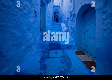 Silhouette einer Dame, die die blaue Treppe in einer Gasse in der Stadt Chefchaouen hochgeht. Stockfoto