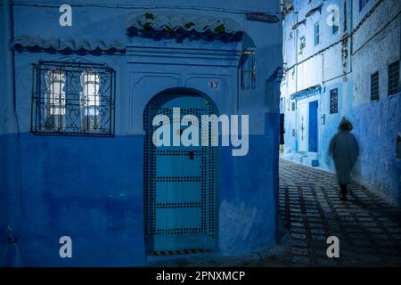 Silhouette eines Mannes mit Djellaba, der nachts durch eine Gasse in Chefchaouen geht. Stockfoto