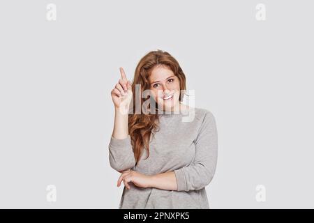 Schöne, fröhliche Frau, die mit dem Finger auf weißen Hintergrund zeigt Stockfoto