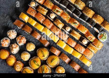Japanische Sushi-Essenssammlung. Maki und Brötchen mit Thunfisch, Lachs, Garnelen, Krabben und Avocado, Käse. Blick von oben auf verschiedene Sushi-Sorten. Regenbogen-Sushi-Brötchen Stockfoto
