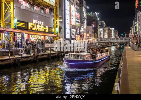 Osaka Nachtleben 2023. April, Menschenmassen im Dotonbori Viertel, während ein Kanalboot voller Menschen durch den Bezirk, Osaka, Japan, Asien fährt Stockfoto