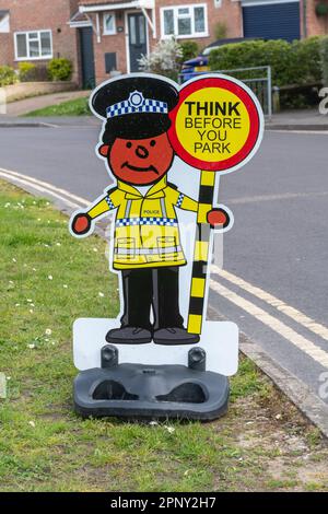 Ein lustiges Schild vor einer Schule mit einem Polizisten und einem Lutscher, die das Schild lesen. Denken Sie daran, bevor Sie parken, England, Großbritannien. Verkehrssicherheit an der Schule Stockfoto