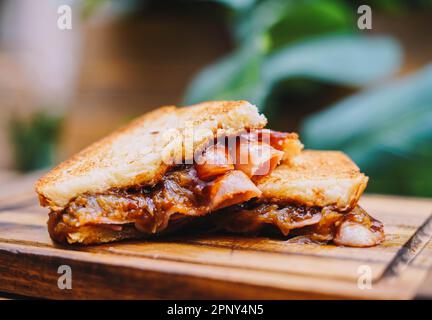 Frühstückssandwich mit Speck, Käse und Tomatensoße auf Holzbrett Stockfoto