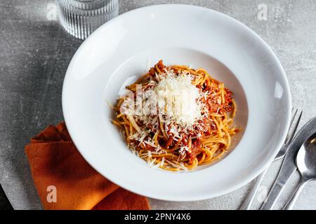 Pasta Bolognese auf einem weißen Teller auf einem hellen Tisch in einem Restaurant Stockfoto