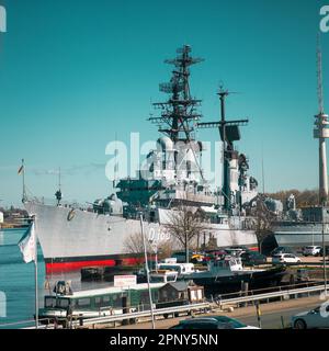 Ein großes Frachtschiff liegt an einem Pier an, mehrere Autos parken an der Seite und ein hoher Turm im Hintergrund Stockfoto