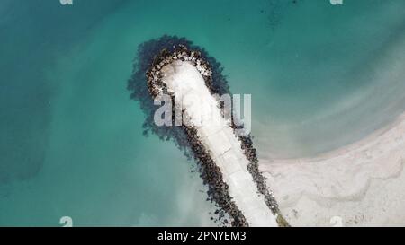 Ein Blick aus der Vogelperspektive auf einen Steinkai, der sich über das Wasser vom Sandstrand bis zum Meer erstreckt Stockfoto