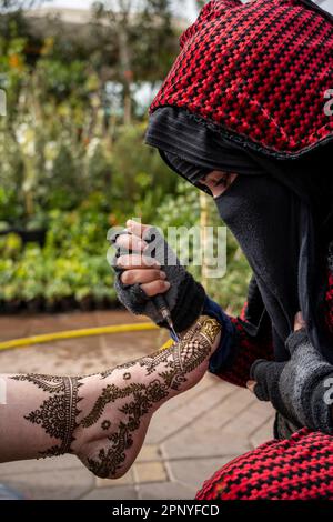 Muslimische Frau, die den Fuß eines Klienten mit Henna dekoriert, auf dem Platz Jemaa el-Fnaa in Marrakesch. Stockfoto