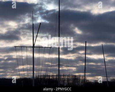 Dunkler, bedeckter Himmel; eine abstrakte Reihe von Yachtmasten und -Takelings bei Sonnenaufgang in Abingdon Marina an der Themse. Stockfoto