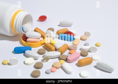 Viele Pillen auf dem Tisch, Nahaufnahme. Tabletten mit unterschiedlichen Formen und Farben sind auf dem Tisch verstreut. Die Pillen sind aus der Flasche gelaufen Stockfoto