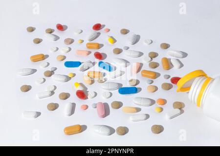 Viele Pillen auf dem Tisch, Nahaufnahme. Tabletten mit unterschiedlichen Formen und Farben sind auf dem Tisch verstreut. Die Pillen sind aus der Flasche gelaufen Stockfoto