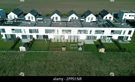 Blick aus der Vogelperspektive auf die warmen, sonnigen Wohnhäuser der Nachbarschaft mit einer Straße und einem Feld. Stockfoto