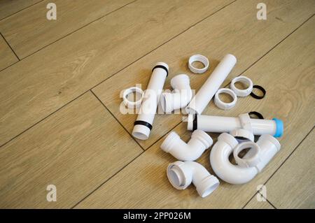 Weiße Kunststoffrohre, Rohre, glatt und gebogen, Armaturen, Flansche, Gummidichtungen. Vor dem Hintergrund beigefarbener Bretter. Platz für das in Stockfoto