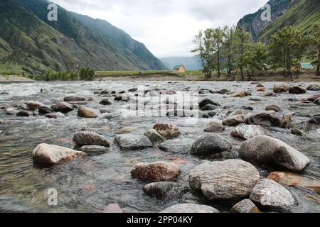 Haus am Ufer des schnellen Flusses Chulyshman, im Altai-Gebirge. Steine im Wasser, grüne Bäume. Erholungszentrum für Touristen. Hochwertige Pho Stockfoto