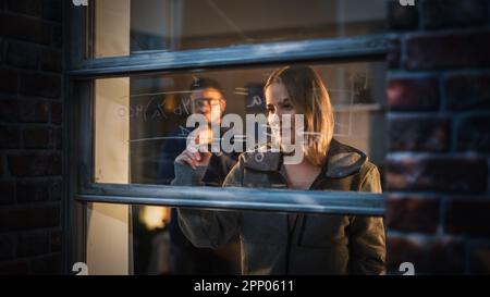 Weißes junges Weibchen, das eine mathematische Gleichung in einem Fenster zu Hause einem männlichen Freund erklärt, indem es entfernbare Glasmarker verwendet. Zwei Multiethnische Zukunftsingenieure Stockfoto