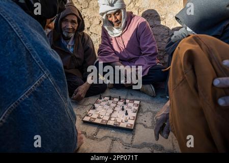 Eine Gruppe von Männern, die auf dem Boden sitzen und in den Straßen des Dorfes Igiouaz Dame spielen. Stockfoto