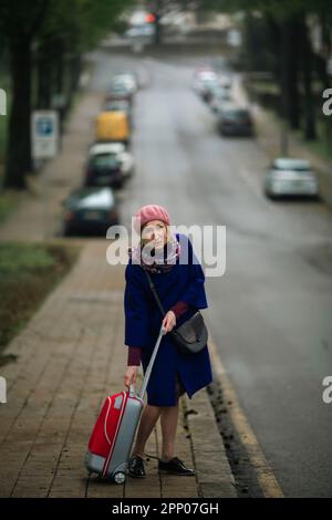 Eine Frau mit einem Koffer läuft die Straße entlang. Stockfoto