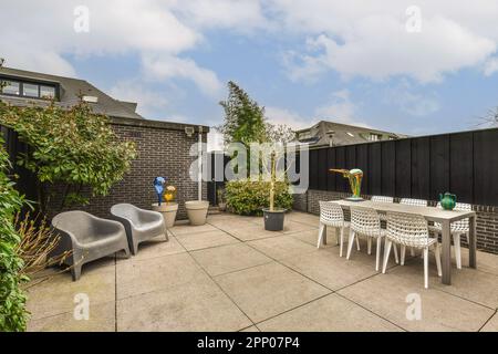 Eine Terrasse mit Stühlen, Tischen und einem Sonnenschirm auf dem Tisch vor einem schwarz umzäunten Hinterhof Stockfoto