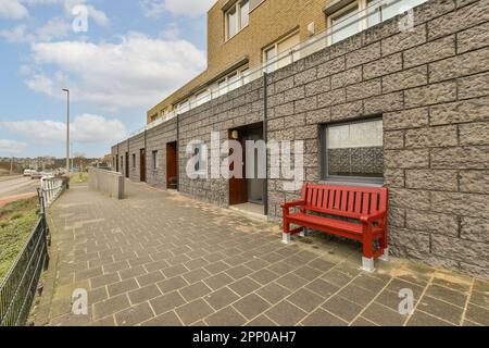 Eine rote Bank vor einem Ziegelgebäude an einer Straßenseite neben einem leeren Parkplatz Stockfoto