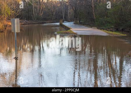 Ein Fußweg und ein Schild sind teilweise von einem nahegelegenen Bach überflutet, der von sintflutartigen Regenfällen überflutet wird. Stockfoto