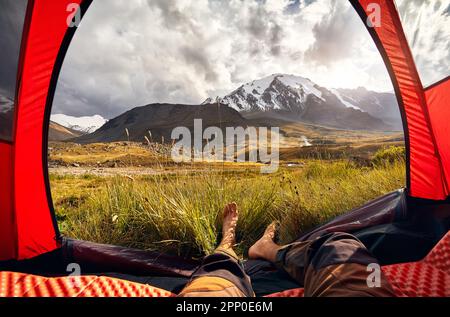 Blick aus dem Inneren eines Zelts und Wanderbeine in das Gebirgstal mit Gletscherlandschaft, pov-Blick Trekking in Zentralasien Kasachstan, Almaty Stockfoto