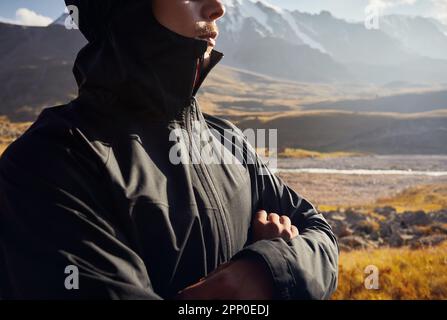 Anonymes Porträt eines jungen Wanderers in schwarzer Jacke, der vor dem wunderschönen Sonnenuntergang im Bergtal steht. Outdoor- und Trekking-Konzept. Stockfoto