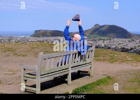 Edinburgh, Schottland, Großbritannien. 21. April 2023 Starke, bläuliche Winde auf dem Gipfel des Blackford Hill, bei denen Besucher darum kämpfen, ihre Wollhüte im Wind wegfliegen zu lassen. Blick über die Dächer der Stadt auf Arthurs Seat. Kredit: Craig Brown/Alamy Live News Stockfoto