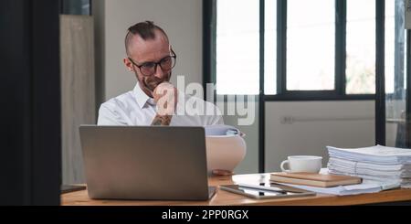 Seriöser Finanzbuchhalter für Papierarbeit im Büro, reifer Mann, der ein Notebook für die Berechnung von Berichten und die Zusammenfassung von Konten verwendet Stockfoto