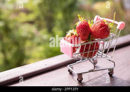 Kleiner Einkaufswagen gefüllt mit rohen, köstlichen Erdbeeren. Concept Shot symbolisiert den Kauf gesunder Lebensmittel oder die Online-Bestellung. Sommer diet.berries in Stockfoto