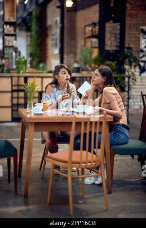 Zwei junge Frauen im Café, die sich unterhalten oder über etwas Ernstes reden. Eine Frau, die ihrem Freund etwas erklärt. Meeting, Studenten, Geschäftskonzept. Stockfoto