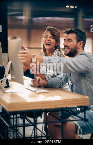 Junge, schöne Kollegen, die bei der Arbeit auf den Bildschirm schauen, über den der pc spricht, und sich glücklich fühlen. Freiberuflich, geschäftlich, Teamwork-Konzept. Stockfoto