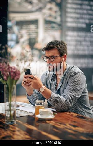 Geschäftsmann im Café, der ein Smartphone mit Kopfhörern benutzt, in einer Kaffeepause. Business, Student, Kaffeepause. Stockfoto