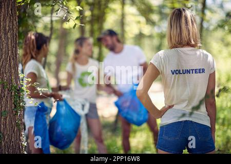 Junge Umweltschützer plaudern, während sie an einem schönen Sommertag Müll im Wald sammeln. Ökologie, Menschen, Pflege Stockfoto