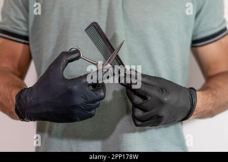 Die Hände eines Friseurs mit schwarzen Handschuhen halten eine Schere an einem Kamm vor weißem Hintergrund Stockfoto