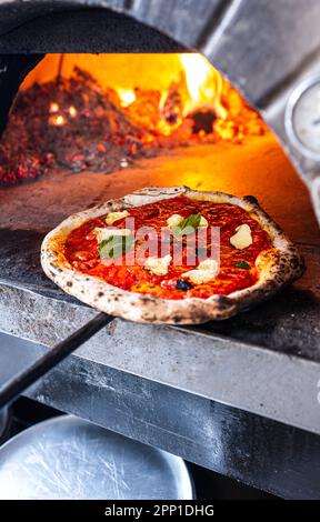 Pizzaiolo holt eine frisch gebackene neapolitanische Margherita Pizza aus dem traditionellen Holzofen. Stockfoto