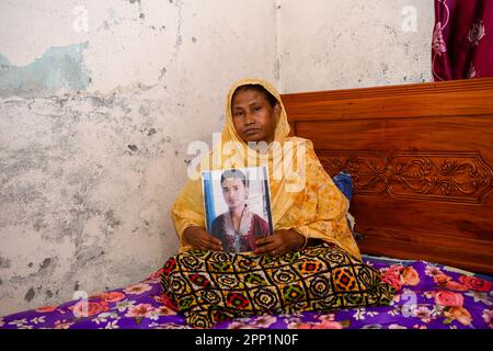 ReNu Begum (55) posiert für ein Porträt mit einem Foto ihres verstorbenen Sohnes Robiul Islam Manik. Vor zehn Jahren am 24. April 2013 wurde die Welt Zeuge einer der schlimmsten Industriekatastrophen der Geschichte, als das Rana Plaza-Gebäude in Bangladesch zusammenbrach, mehr als 1.100 Menschen tötete und 2500 weitere verletzte. Die Tragödie hat weltweit Schockwellen ausgelöst und Sorgen über die unsicheren Arbeitsbedingungen im boomenden RMG-Sektor (Ready-Made Garment) in Bangladesch ausgelöst. In dem achtstöckigen Gebäude waren mehrere Fabriken untergebracht, in denen Kleidung für globale Marken wie Primark, Mango und Benetton hergestellt wurde. Das Buildin Stockfoto