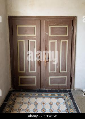 Alte Holztüren in einem alten Haus aus dem Jahre 1900. Raue Oberflächen der Innenwand. Die Fliesen auf dem Foor sind antik. Früher gab es Toiletten. Stockfoto