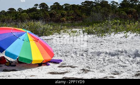 Farbenfroher Regenschirm unter blauem Himmel am Sandstrand des Ozeans Stockfoto