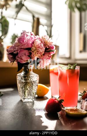 Gefrorener Smoothie mit Erdbeer- und Minzbonbons, ultimativer Sommerspaß in der Nähe eines Straußes frischer Pfingstrosen Stockfoto