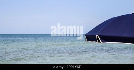 Farbenfroher Regenschirm unter blauem Himmel am Sandstrand des Ozeans Stockfoto